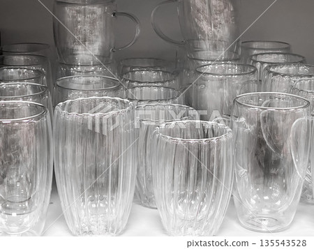 Multiple empty clear glass cups arranged on a shelf. 135543528