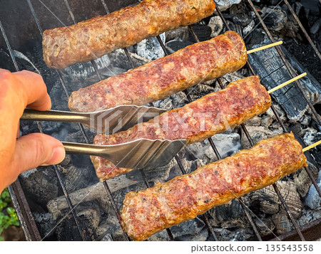 Grilling kebabs over charcoal with tongs on a barbecue. 135543558