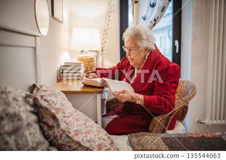 Senior woman relaxing and reading while preparing for sleep. 135544063
