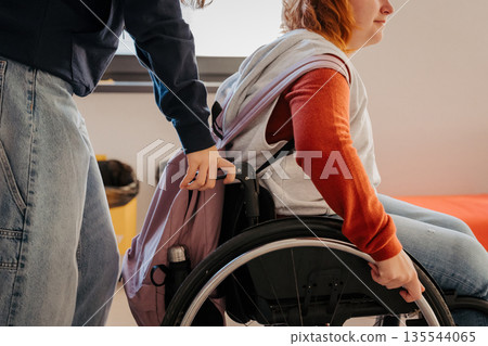 Schoolmate pushing girl in wheelchair on school hallway. Schoolmate pushing girl in wheelchair on school hallway. 135544065