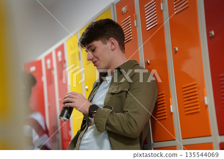 Teen student drinking an energy drink in school hallway. 135544069