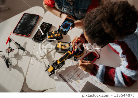 High school students working on robotics project, using online AI app to answer questions. 135544075