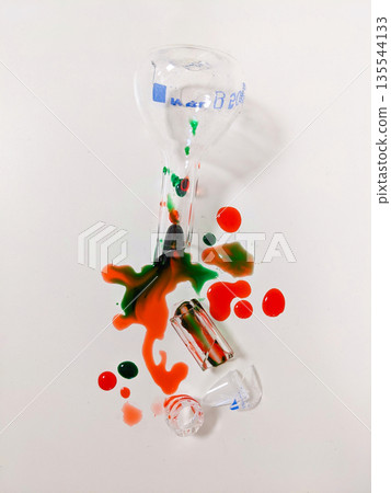A broken beaker and other lab equipment are shown with spilled red and green liquids, creating an abstract pattern A broken beaker and other lab equipment are shown with spilled red and green liquids, creating an abstract pattern 135544133