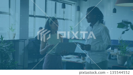 Discussing woman holding laptop and man checking smartphone in open office, with notes and plants Discussing woman holding laptop and man checking smartphone in open office, with notes and plants 135544552