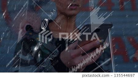 Standing woman in black top holding smartphone at graffiti wall, showing sensor, charts, graphs 135544697