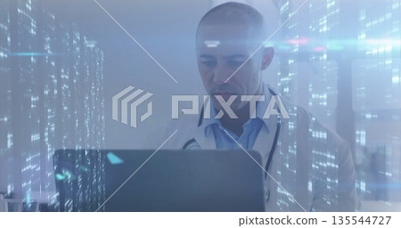 Doctor wearing labcoat and stethoscope working on laptop in clinic office, with holographic overlay 135544727
