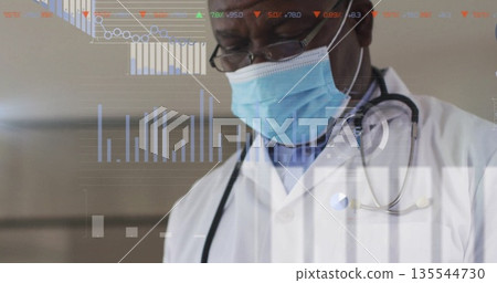 Senior Black male doctor analyzing digital patient data in clinical hallway, with stethoscope mask 135544730