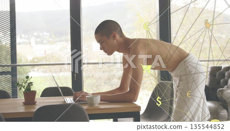 Leaning towel-wrapped man typing on laptop at home, with plant mug sofa and digital overlay 135544852