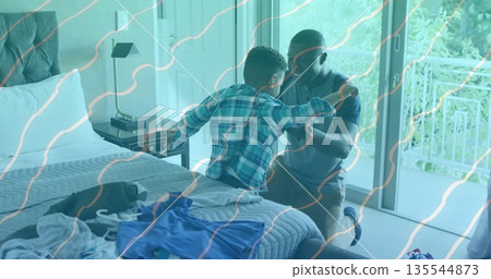 Interacting father kneeling beside son in plaid shirt sitting in bedroom by sliding glass door Interacting father kneeling beside son in plaid shirt sitting in bedroom by sliding glass door 135544873