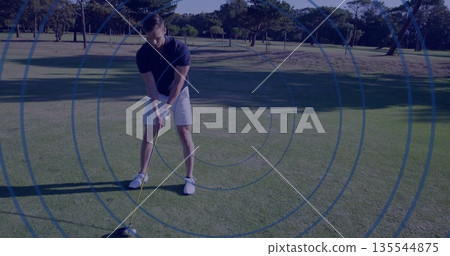 Preparing adult golfer gripping driver over tee on manicured fairway, with blue ring overlay 135544875