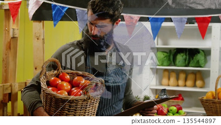 Vendor wearing apron reviewing clipboard and holding basket of tomatoes in market stall, copy space 135544897