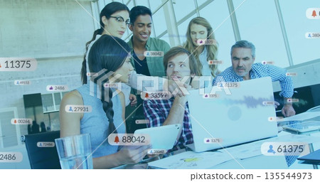 Analyzing team of six working on laptops and tablet at modern office, with floating media icons 135544973