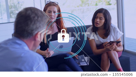 Collaborating professionals sitting on sofa in office lounge, using laptop smartphone with report 135545006