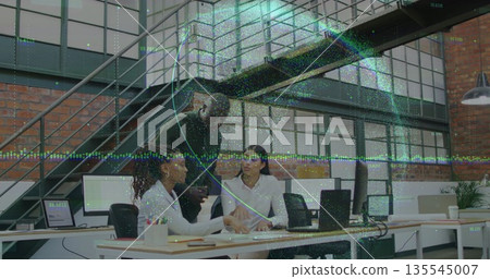 Collaborating trio reviewing printed documents at loft desk with brick walls, laptops, notebooks 135545007