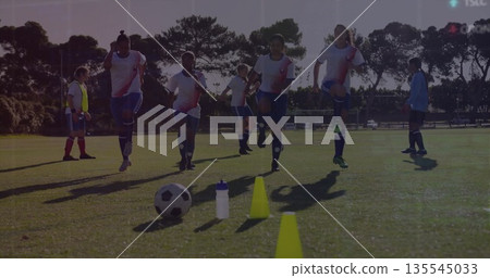 Jogging soccer players performing warm up drills on grassy pitch, with cones, ball and water bottle Jogging soccer players performing warm up drills on grassy pitch, with cones, ball and water bottle 135545033