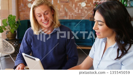Two colleagues reviewing white tablet on wooden table at lounge, with coffee cup and teal sofa Two colleagues reviewing white tablet on wooden table at lounge, with coffee cup and teal sofa 135545059