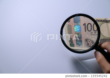 有人用放大鏡檢查一張10000日圓鈔票上的全息圖。 135545242
