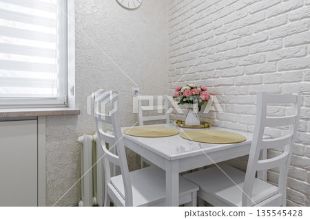 Cozy dining nook with white wooden table and floral decor Cozy dining nook with white wooden table and floral decor 135545428