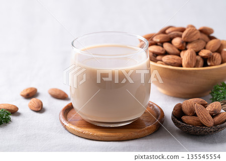 Glass of almond milk and almond nuts on white fabric background 135545554