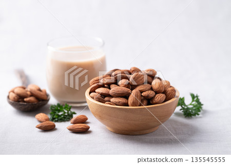 Glass of almond milk and almond nuts on white fabric background 135545555