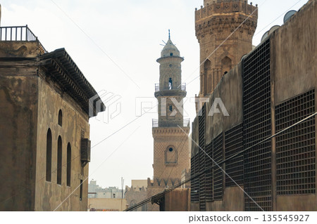 Historic Qalawun Complex in Cairo, featuring intricate architecture, tall minarets, and domes under a blue sky with clouds. A significant cultural landmark on Al-Muizz Street. Historic Qalawun Complex in Cairo, featuring intricate architecture, tall minarets, and domes under a blue sky with clouds. A significant cultural landmark on Al-Muizz Street. 135545927