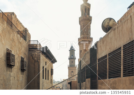 Historic Qalawun Complex in Cairo, featuring intricate architecture, tall minarets, and domes under a blue sky with clouds. A significant cultural landmark on Al-Muizz Street. 135545931