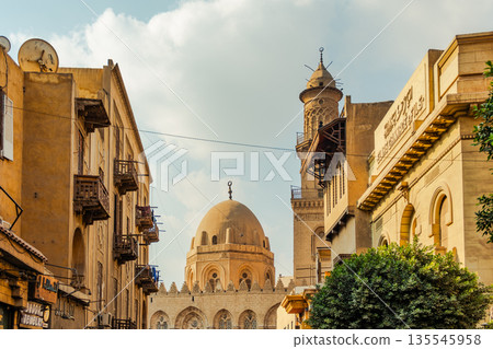 Historic Qalawun Complex in Cairo, featuring intricate architecture, tall minarets, and domes under a blue sky with clouds. A significant cultural landmark on Al-Muizz Street. Historic Qalawun Complex in Cairo, featuring intricate architecture, tall minarets, and domes under a blue sky with clouds. A significant cultural landmark on Al-Muizz Street. 135545958