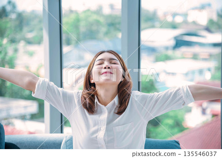Relax woman yawning sitting on cozy sofa in apartment. Asian woman relax stretching arm laziness comfortable in living room. Happiness girl lifestyles sitting at home living room. Stretching arm relax 135546037
