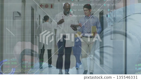 Walking medical team discussing data in hospital corridor, with tablet, folder and overlay charts Walking medical team discussing data in hospital corridor, with tablet, folder and overlay charts 135546331