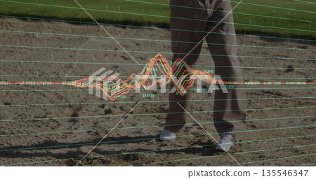 Standing male wearing gray slacks and white sneakers at sports field track, with data graph overlay 135546347