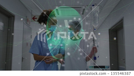 Walking patient gripping IV pole with nurse guiding in hospital corridor, digital face scan overlay 135546387