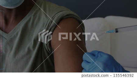 Injecting masked man getting vaccine in exam room with syringe needle, blue gloves, padded couch 135546392