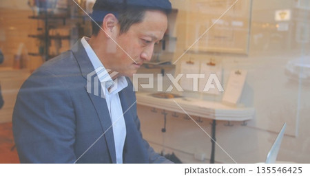Typing man in gray suit with white shirt using silver laptop at cafe table, with clipboards 135546425