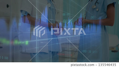 Discussing patient data two women in scrubs with stethoscopes in ward, with digital charts overlay 135546435