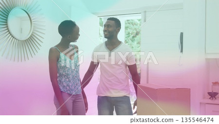 Smiling couple standing near open front door in entrance area, with sunburst mirror and moving box Smiling couple standing near open front door in entrance area, with sunburst mirror and moving box 135546474
