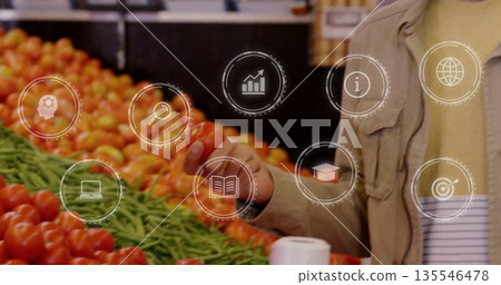 Selecting mid-adult man reaching for tomato at market with green beans, digital icons, copy space 135546478