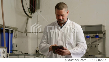Inspecting equipment technician wearing lab coat using tablet in facility, with filter housings 135546534