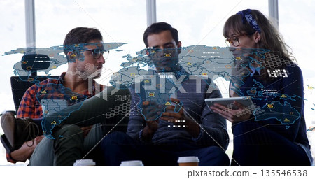 Three professionals discussing data sitting in office lounge, with devices, coffee and map overlay 135546538