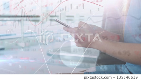 Woman in blue dress checking stock charts on smartphone at office desk, with monitor, copy space Woman in blue dress checking stock charts on smartphone at office desk, with monitor, copy space 135546619