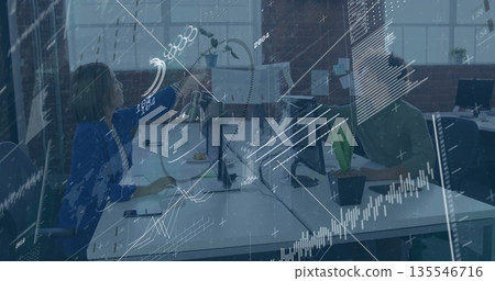 Woman in navy blazer handing document to man in green shirt in loft office, with monitors 135546716