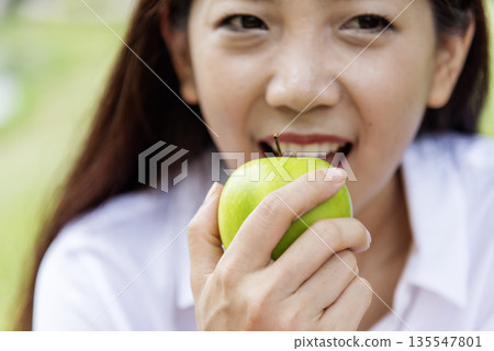 young asian woman eating Apple Healthy. Girl workout holding organic apple fruit healthy lifestyle. Wellness Asian women eat red apple smile face look at camera. Beauty health care lifestyle concept 135547801