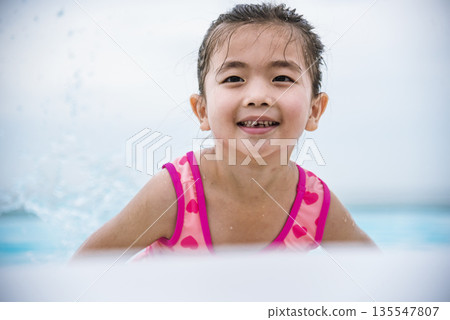Portrait Girl in pink swimsuit playful in swimming pool summer time with pink swimwear, blue water at hotel swimming pool outdoor. Toddler girl Kid smile laugh look at camera. Happy girl swim playful 135547807