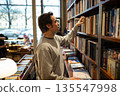 Curious focused man booklover picking hardcover book from bookshelf in modern bookstore library. 135547998