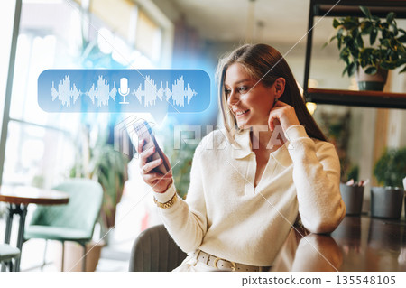 Woman using smartphone to send voice message while sitting in cafe during the day 135548105