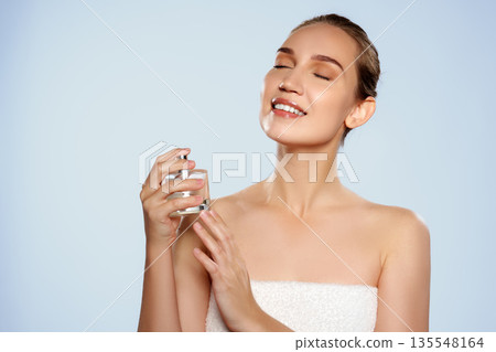 Woman holding a perfume bottle and enjoying a scent in a bright setting 135548164
