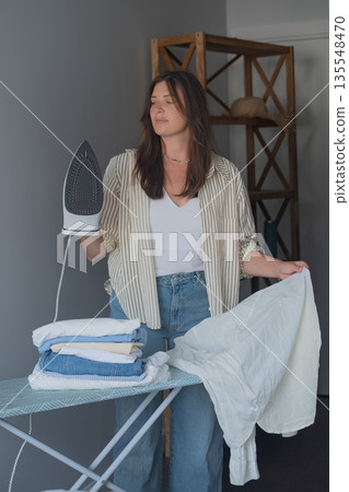 Woman caring for wardrobe before work portrait holding iron in hand wearing casual clothes jeans and shirt 135548470