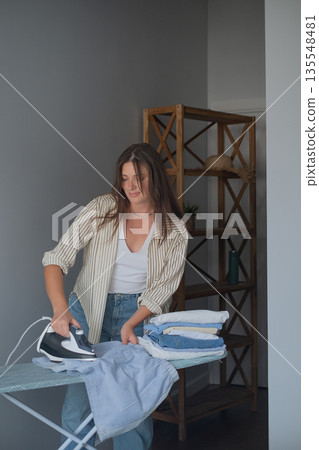 Home routine and quality clothing care with woman smoothing clothes with a steam iron for a neat organized wardrobe Home routine and quality clothing care with woman smoothing clothes with a steam iron for a neat organized wardrobe 135548481
