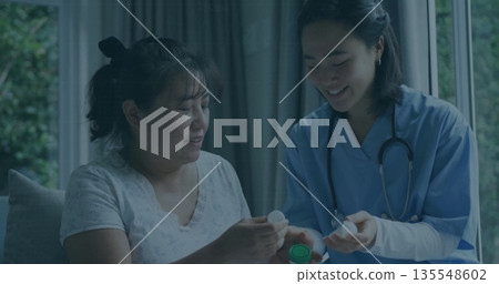 Holding pill bottle, nurse in blue scrubs, stethoscope guiding patient examining cap in living room Holding pill bottle, nurse in blue scrubs, stethoscope guiding patient examining cap in living room 135548602