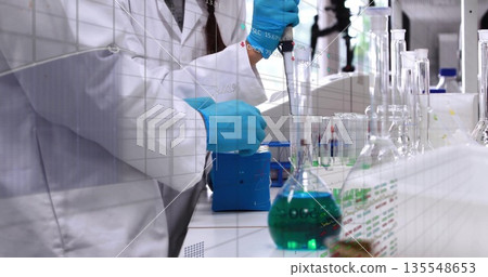 Using micropipette scientist wearing lab coat transferring green solution into flask at lab bench Using micropipette scientist wearing lab coat transferring green solution into flask at lab bench 135548653