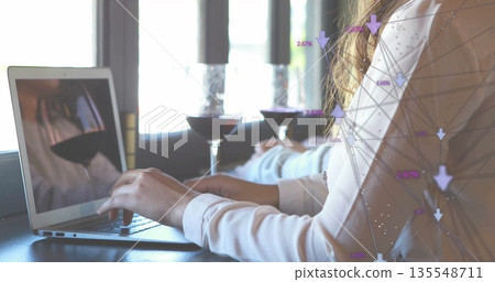 Woman in white blouse typing on laptop in cafe, with wine glasses, candlesticks, network graphics 135548711